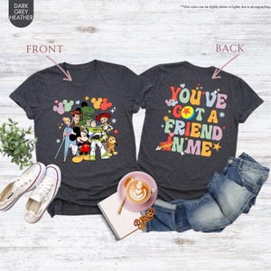 May include: Dark grey heather t-shirts with colorful graphics. One shirt features Disney characters, including Mickey Mouse and Toy Story characters. The other shirt displays the text "You've Got a Friend in Me" in a retro font.