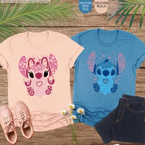 May include: Two t-shirts, one peach and one teal, each featuring a cartoon character design. The peach shirt has a pink character design, and the teal shirt has a blue character design. The shirts are displayed with jeans and shoes.