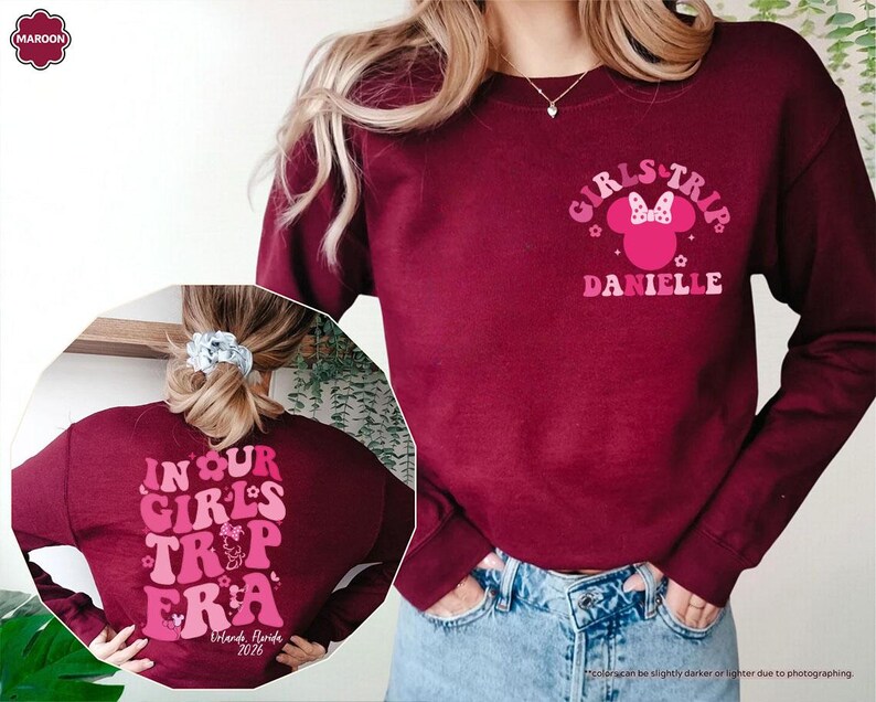 Peut inclure: Sweat-shirt bordeaux avec l'inscription "GIRLS TRIP DANIELLE" sur le devant et "IN OUR GIRLS TRIP ERA Orlando, Florida 2026" au dos. Le motif comprend une silhouette de Minnie Mouse et des &eacute;l&eacute;ments floraux. Le sweat-shirt est &agrave; manches longues et col rond.