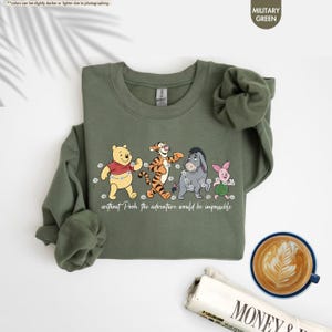 Puede incluir: Sudadera verde militar con Winnie the Pooh, Tigger, Eeyore y Piglet. La frase "without Pooh the adventure would be impossible" est&aacute; impresa debajo de los personajes. La sudadera tiene cuello redondo y mangas largas.