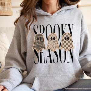 May include: A sport grey hooded sweatshirt featuring the black text SPOOKY SEASON and three ghost illustrations. The ghosts have distinct patterns: one with a green camouflage print, one with a brown leopard print, and one with a tan checkerboard pattern.