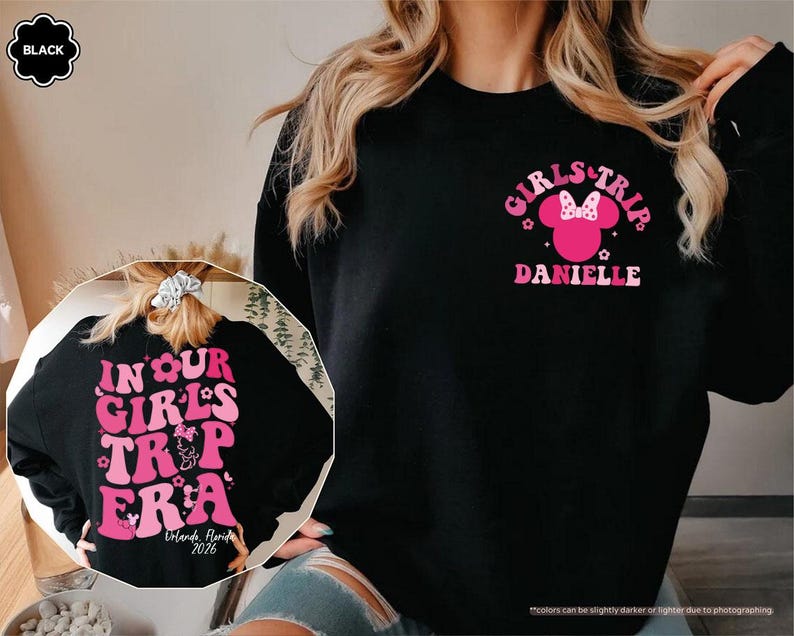 Peut inclure: Sweat-shirt noir avec texte et graphiques roses. Le devant affiche "GIRLS TRIP" avec une t&ecirc;te de Minnie Mouse et le nom "DANIELLE". Le dos indique "IN OUR GIRLS TRIP ERA" avec "Orlando, Florida 2026".