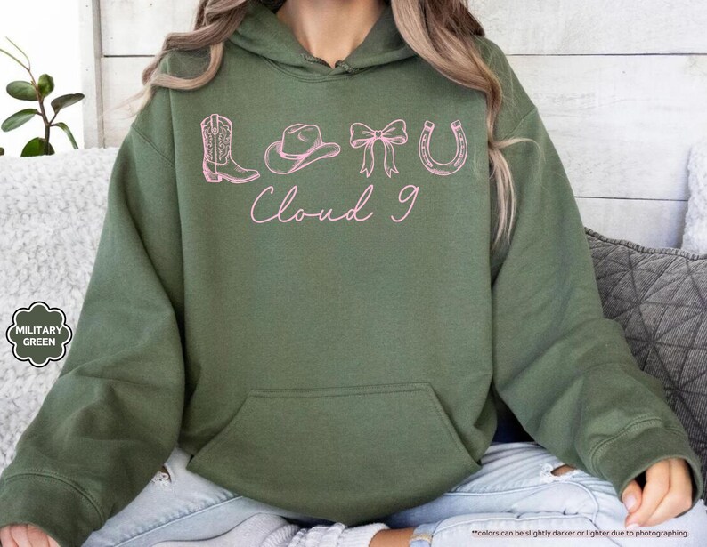 May include: Military green hoodie with a front pocket and a drawstring hood. The front features pink line art of a cowboy boot, hat, bow, horseshoe, and the words "Cloud 9".