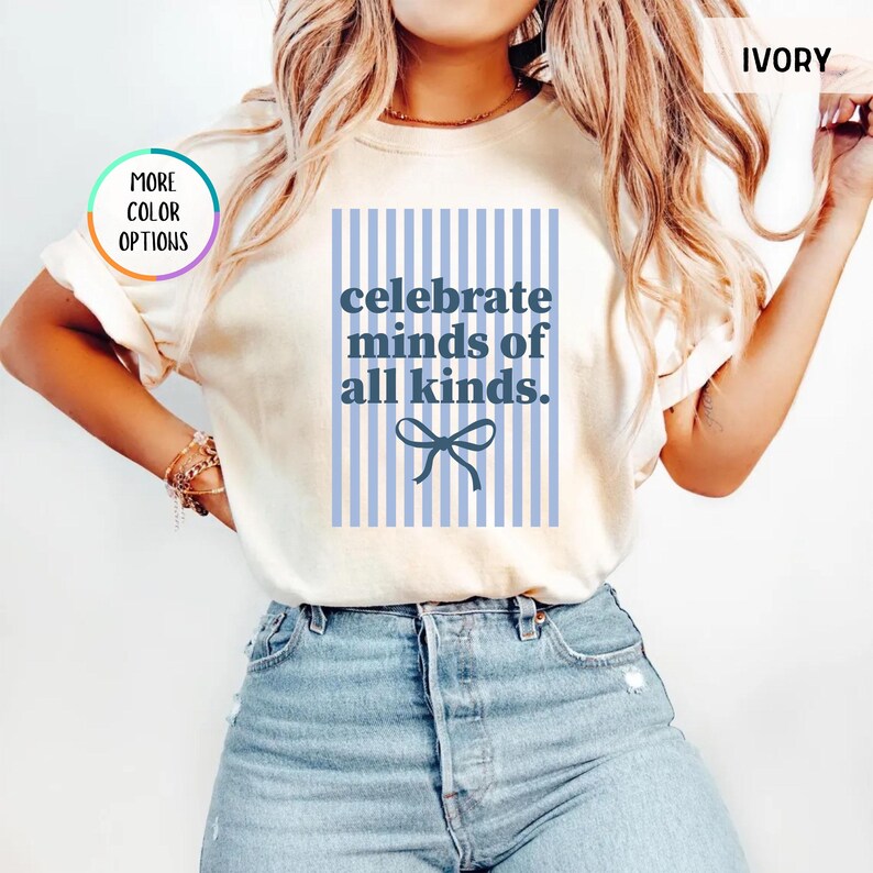 Puede incluir: Camiseta de color marfil con el texto azul "celebrate minds of all kinds" sobre un fondo a rayas azul claro. Un lazo azul est&aacute; debajo del texto. La camiseta tiene mangas cortas.