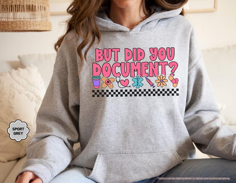 Puede incluir: Una sudadera gris claro con el texto "BUT DID YOU DOCUMENT?" en rosa y blanco. El dise&ntilde;o incluye gr&aacute;ficos de tem&aacute;tica m&eacute;dica como una taza de caf&eacute;, una venda, un estetoscopio, un coraz&oacute;n y una jeringa. La sudadera tiene un bolsillo delantero y una capucha con cord&oacute;n.