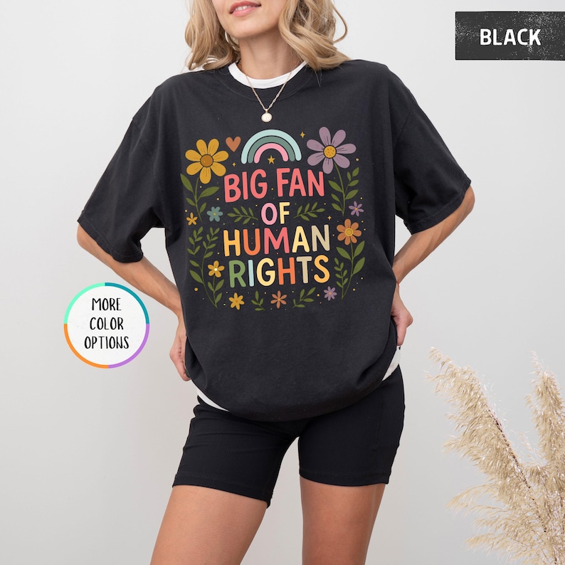 May include: Black t-shirt with the text "BIG FAN OF HUMAN RIGHTS" in colorful letters and floral accents. The design includes a rainbow, flowers, and leaves. The shirt is a casual, oversized fit.
