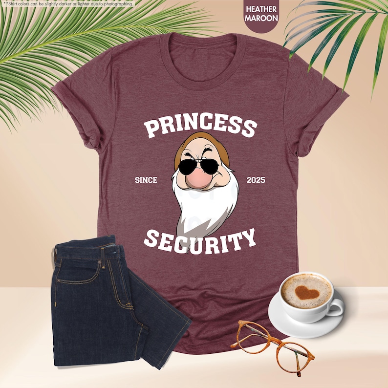May include: Heather maroon t-shirt with a white graphic of a cartoon character wearing sunglasses and a beard. The text "Princess Security" is printed on the shirt with the years "Since 2025".