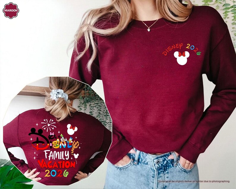 Puede incluir: Una sudadera de cuello redondo color granate con un peque&ntilde;o icono de cabeza de Mickey Mouse en blanco con un lazo rojo y el texto Disney 2026 en el pecho. La parte trasera muestra un gr&aacute;fico grande con personajes de Disney, fuegos artificiales y el texto Disney Family Vacation 2026.