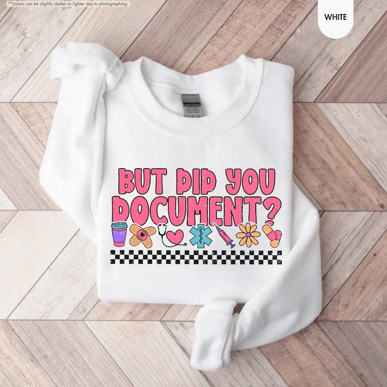 Puede incluir: Sudadera blanca con la frase "BUT DID YOU DOCUMENT?" en letras rosas y naranjas. El dise&ntilde;o incluye gr&aacute;ficos m&eacute;dicos como una venda, un estetoscopio y una jeringa, con un borde a cuadros blanco y negro.