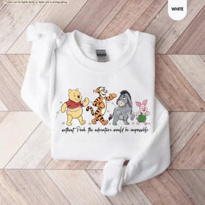 Puede incluir: Sudadera blanca de cuello redondo con un gr&aacute;fico de Winnie the Pooh, Tigger, Eeyore y Piglet. Los personajes caminan juntos con una cadena de luces. El texto "without Pooh, the adventure would be impossible" est&aacute; debajo.