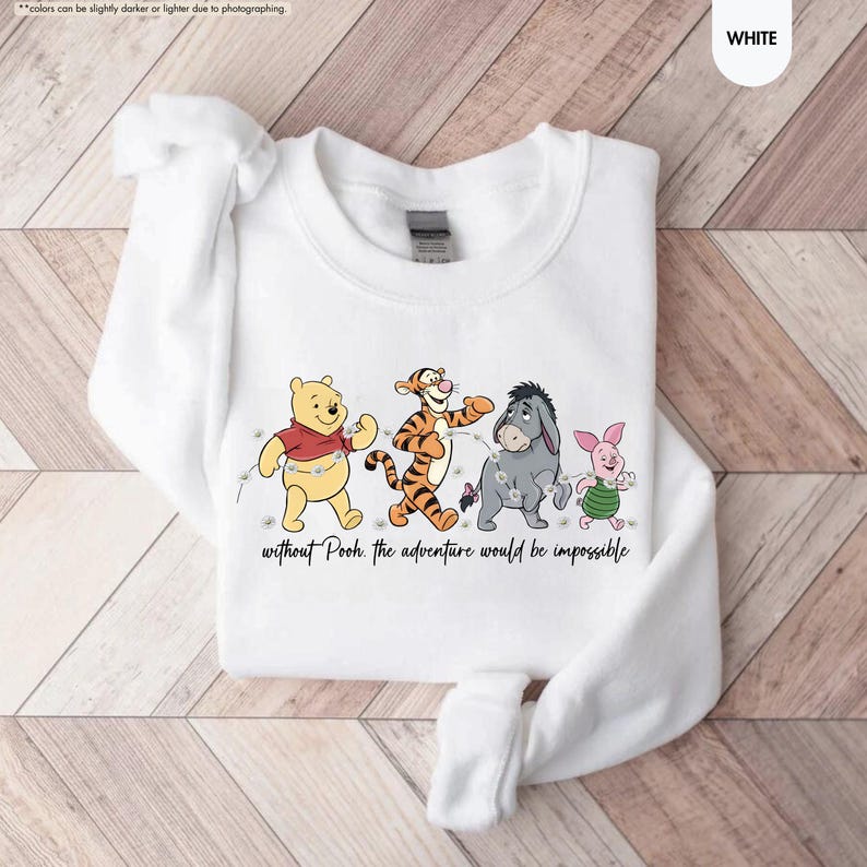 Puede incluir: Sudadera blanca de cuello redondo con un gr&aacute;fico de Winnie the Pooh, Tigger, Eeyore y Piglet. Los personajes caminan juntos con una cadena de luces. El texto "without Pooh, the adventure would be impossible" est&aacute; debajo.