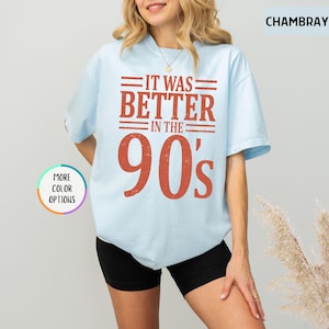 May include: A light blue short-sleeve t-shirt featuring the text IT WAS BETTER IN THE 90's in a distressed red font. The shirt has a crew neckline and a relaxed fit. A small circular graphic on the left side displays the text MORE COLOR OPTIONS.