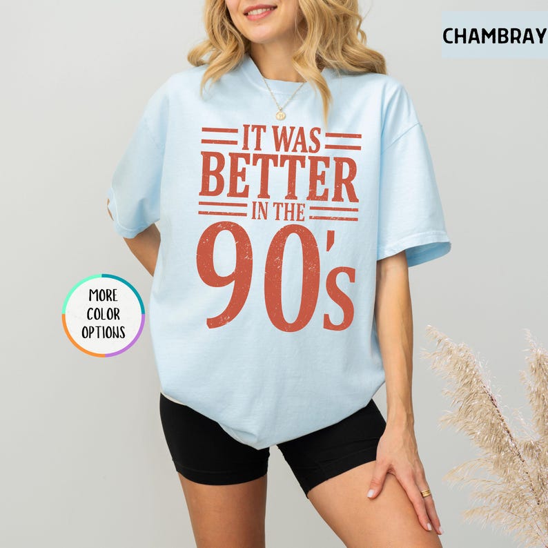 May include: A light blue short-sleeve t-shirt featuring the text IT WAS BETTER IN THE 90's in a distressed red font. The shirt has a crew neckline and a relaxed fit. A small circular graphic on the left side displays the text MORE COLOR OPTIONS.