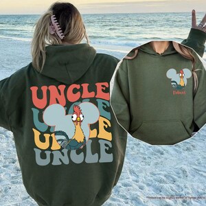 May include: A military green hoodie with the word "UNCLE" in colorful retro font on the back. A cartoon rooster is featured in a Mickey Mouse-shaped design. The front of the hoodie has a similar design with the word "Dobest".