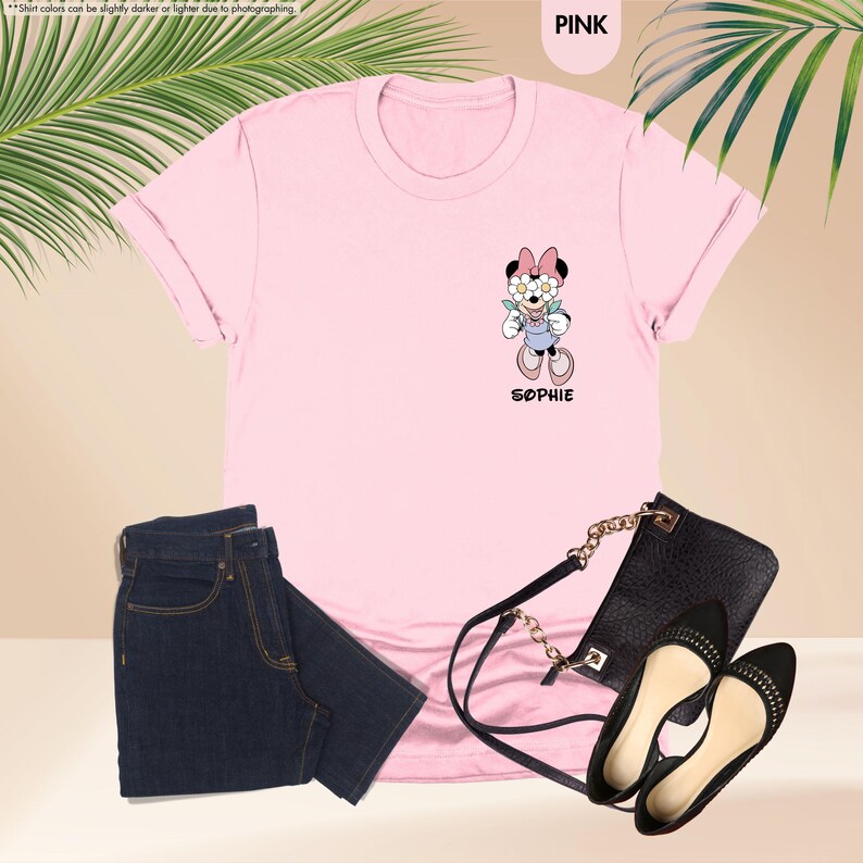 May include: A pink t-shirt with a Minnie Mouse graphic, paired with dark blue jeans, a black purse, and black flats. The Minnie Mouse graphic has the name "Sophie" below it.
