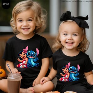 Puede incluir: Dos ni&ntilde;os con camisetas negras con un gr&aacute;fico colorido de Lilo y Stitch. El gr&aacute;fico muestra a Lilo con un vestido rojo y a Stitch en azul. Los ni&ntilde;os sonr&iacute;en y est&aacute;n sentados juntos. Las camisetas son de manga corta.