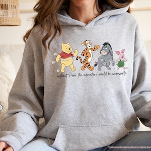 Puede incluir: Sudadera con capucha gris deportivo con un gr&aacute;fico de Winnie the Pooh, Tigger, Eeyore y Piglet caminando juntos. El texto "without Pooh the adventure would be impossible" est&aacute; impreso debajo de los personajes. La sudadera tiene un bolsillo delantero y una capucha con cord&oacute;n.