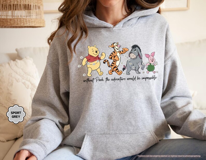 Puede incluir: Sudadera con capucha gris deportivo con un gr&aacute;fico de Winnie the Pooh, Tigger, Eeyore y Piglet caminando juntos. El texto "without Pooh the adventure would be impossible" est&aacute; impreso debajo de los personajes. La sudadera tiene un bolsillo delantero y una capucha con cord&oacute;n.