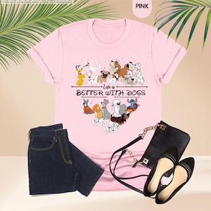 May include: Pink t-shirt with a heart-shaped graphic of various cartoon dogs and the text "Life is Better With Dogs." The shirt is paired with dark blue jeans, a black purse, and black flats.