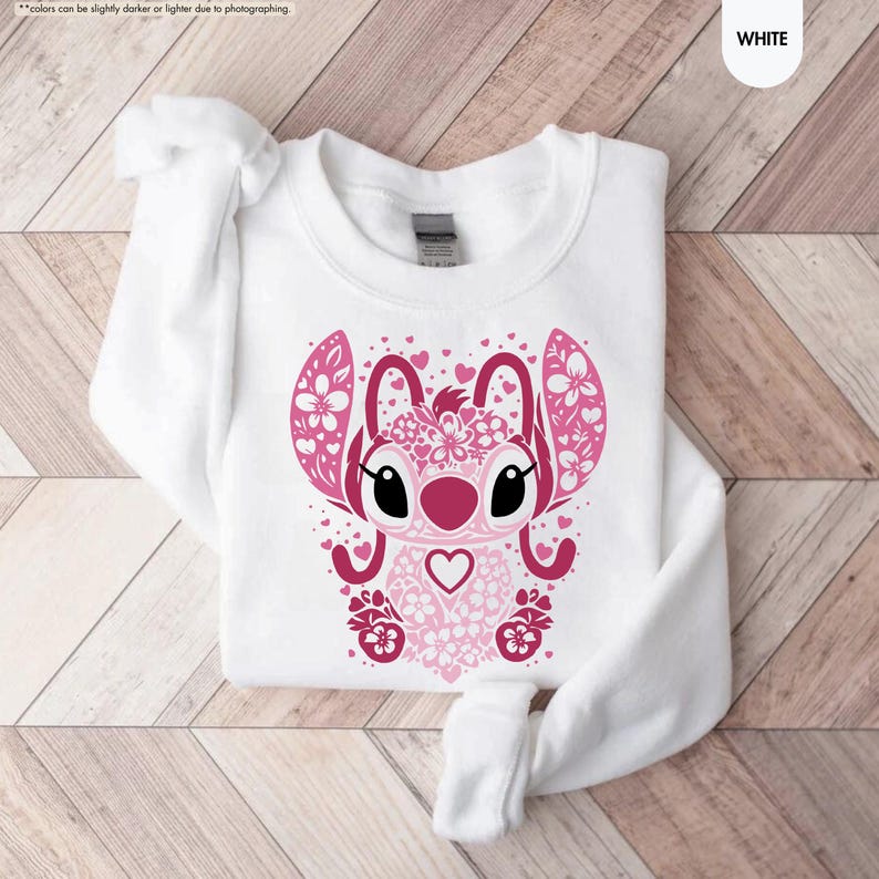May include: White sweatshirt featuring a pink graphic of a cartoon character with large ears, floral accents, and heart details. The design is centered on the front of the long-sleeved top. The word "WHITE" is in the upper right corner.
