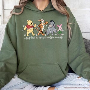 Puede incluir: Sudadera con capucha verde militar con un gr&aacute;fico de Winnie the Pooh, Tigger, Eeyore y Piglet. El texto "without Pooh the adventure would be impossible" est&aacute; impreso debajo. La sudadera tiene un bolsillo delantero.