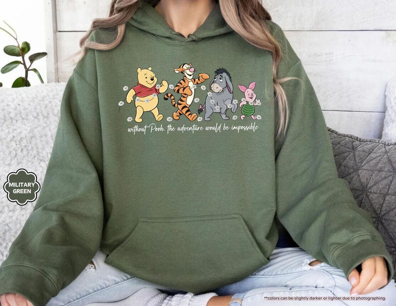 Puede incluir: Sudadera con capucha verde militar con un gr&aacute;fico de Winnie the Pooh, Tigger, Eeyore y Piglet. El texto "without Pooh the adventure would be impossible" est&aacute; impreso debajo. La sudadera tiene un bolsillo delantero.