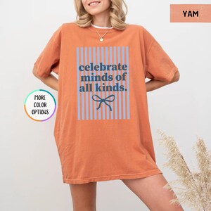 Puede incluir: Camiseta naranja con el texto azul "celebrate minds of all kinds" dentro de un rect&aacute;ngulo a rayas azules y un lazo azul. La camiseta de manga corta tiene un corte holgado. El color es similar al &ntilde;ame.