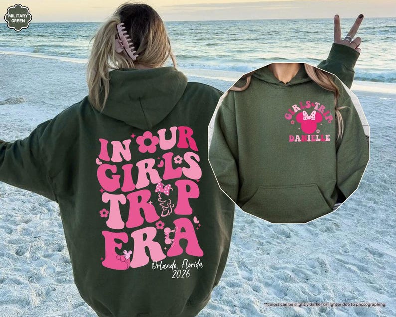 Peut inclure: Un sweat &agrave; capuche vert olive avec un motif rose et blanc au dos indiquant "IN OUR GIRLS TRIP ERA" avec "Orlando, Florida 2026" en dessous. Un motif plus petit sur le devant indique "GIRLS TRIP" avec un design Minnie Mouse.