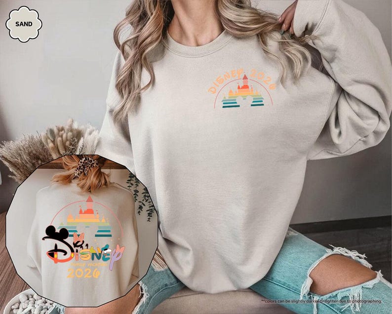 May include: Sand-colored sweatshirt with a Disney 2020 graphic. The design features a castle, rainbow, and text. The sweatshirt is a neutral color and has a crew neck.