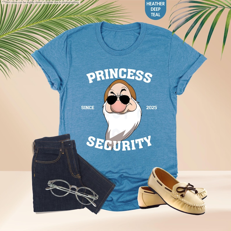 May include: A blue t-shirt with a white graphic of a cartoon character wearing sunglasses and a beard. The text "PRINCESS" is above the character and "SECURITY" is below. The text "SINCE" is to the left of the character and "2025" is to the right.