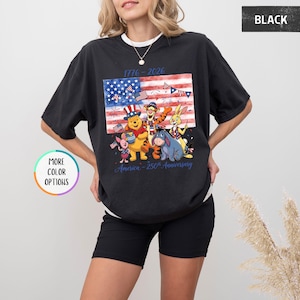 May include: Black t-shirt featuring a colorful graphic of Winnie the Pooh and friends in front of an American flag. The shirt includes the text "1776-2026" and "America - 250th Anniversary". Additional color options are available.