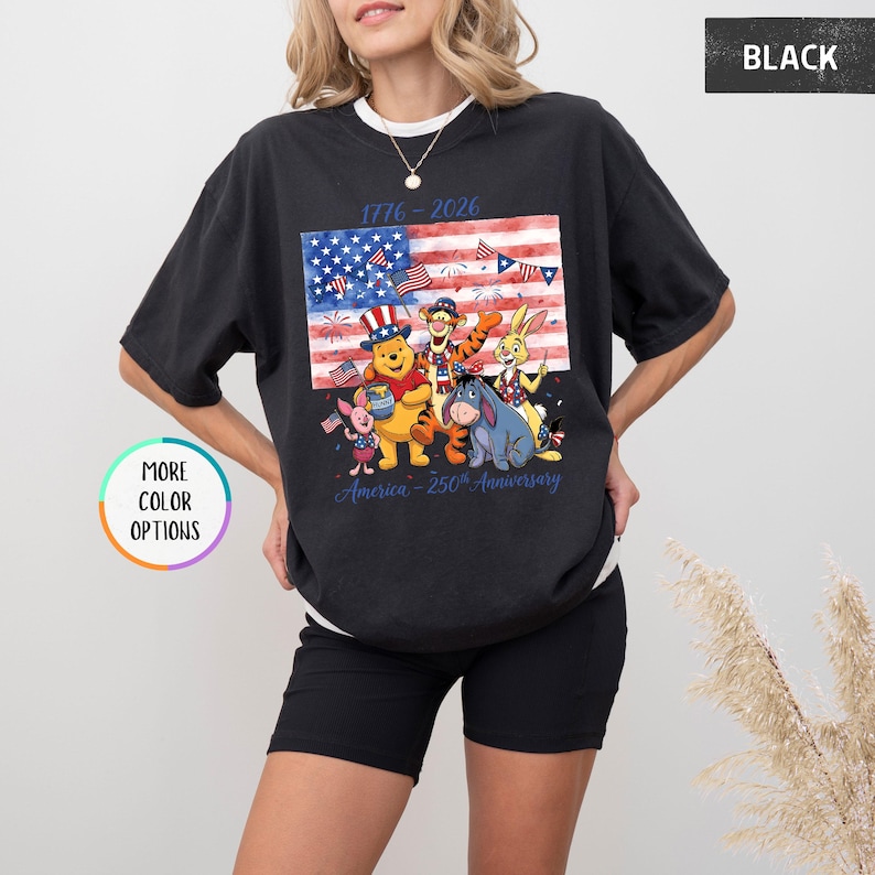 May include: Black t-shirt featuring a colorful graphic of Winnie the Pooh and friends in front of an American flag. The shirt includes the text "1776-2026" and "America - 250th Anniversary". Additional color options are available.
