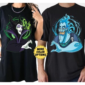Puede incluir: Camisetas negras con ilustraciones de dibujos animados de Mal&eacute;fica y Hades. Mal&eacute;fica se representa con un fondo morado y verde, mientras que Hades tiene un dise&ntilde;o azul y blanco. Las camisetas tienen el texto "MORE COLOR OPTIONS" en un c&iacute;rculo amarillo.