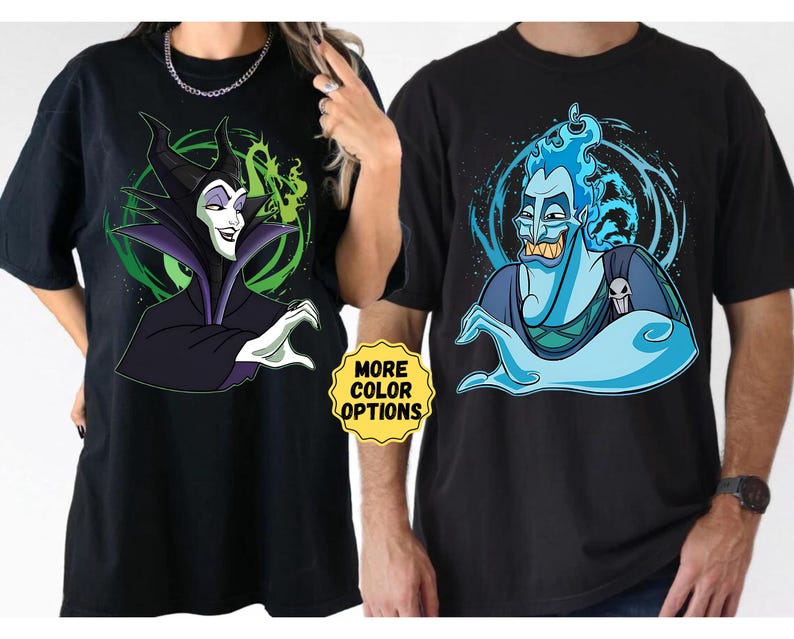 Puede incluir: Camisetas negras con ilustraciones de dibujos animados de Mal&eacute;fica y Hades. Mal&eacute;fica se representa con un fondo morado y verde, mientras que Hades tiene un dise&ntilde;o azul y blanco. Las camisetas tienen el texto "MORE COLOR OPTIONS" en un c&iacute;rculo amarillo.