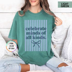 Puede incluir: Camiseta verde claro con el texto "celebrate minds of all kinds" en un dise&ntilde;o de rayas azules. La camiseta tiene un corte holgado y mangas cortas. El texto est&aacute; en una fuente sans-serif.