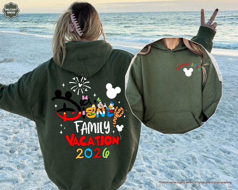 Puede incluir: Una sudadera con capucha de color verde militar que presenta un gr&aacute;fico grande en la espalda con el texto Disney Family Vacation 2026, personajes de dibujos animados y fuegos artificiales. El pecho muestra un icono de Mickey Mouse y Disney 2026.