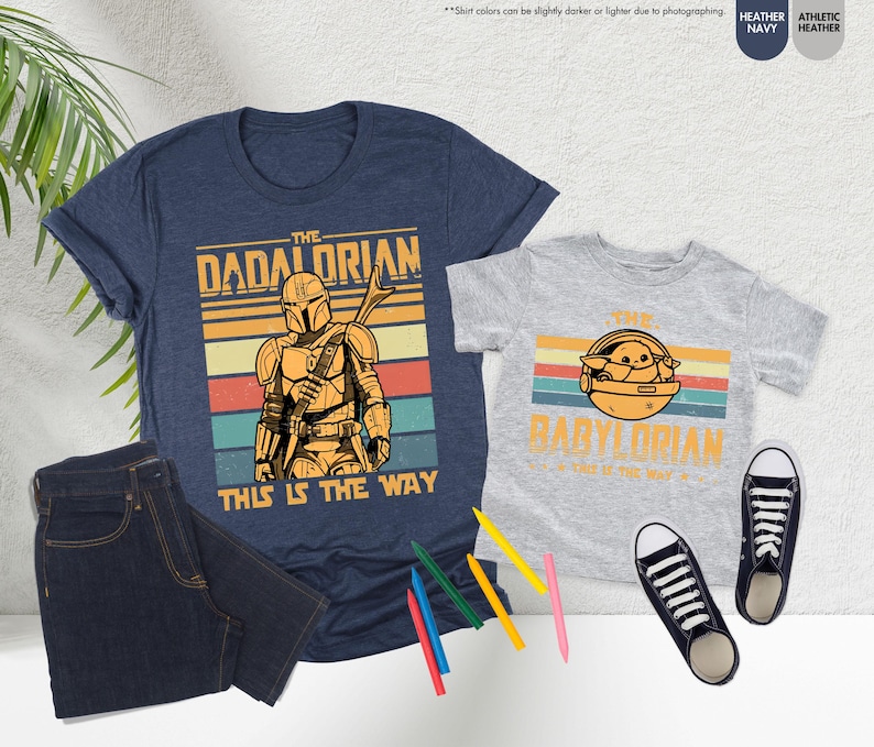 Puede incluir: Dos camisetas, una azul marino y otra gris jaspeado, con gr&aacute;ficos a juego. La camiseta azul marino dice "The Dadalorian" y "This is the Way". La camiseta gris dice "The Babylorian" y "This is the Way". Tambi&eacute;n se ven unos vaqueros oscuros y zapatillas negras.