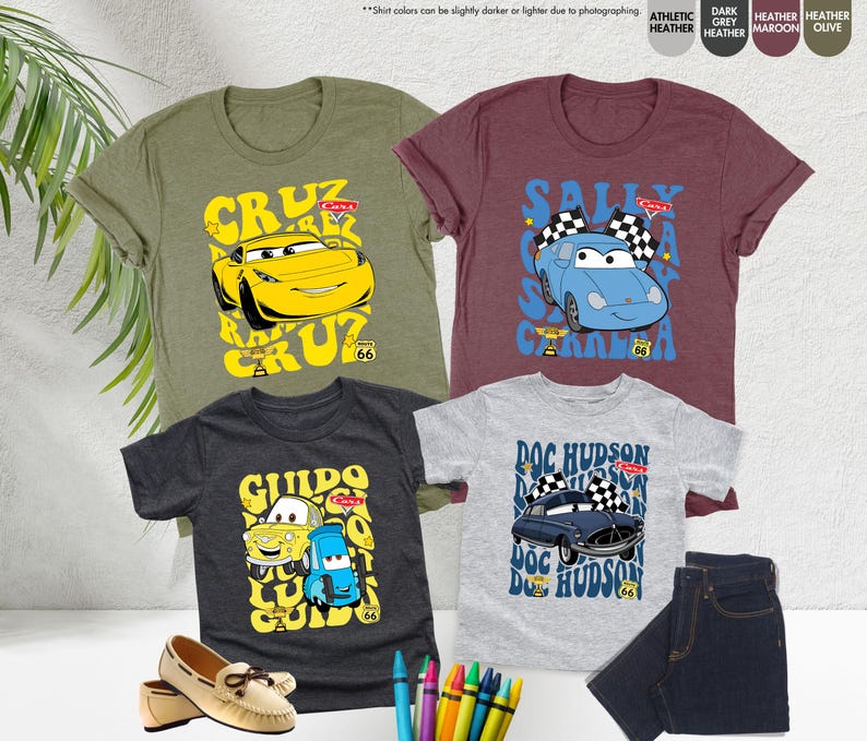 May include: Four short-sleeved t-shirts in olive green, maroon, dark grey, and heather grey, each with a cartoon car design. The shirts feature the names "Cruz", "Sally", "Guido", and "Doc Hudson" and the Route 66 logo.