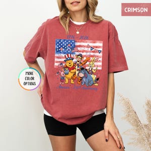 May include: Crimson-colored t-shirt featuring a graphic of Winnie the Pooh and friends celebrating the American flag. The shirt includes the text "1776-2026" and "America - 250th Anniversary".