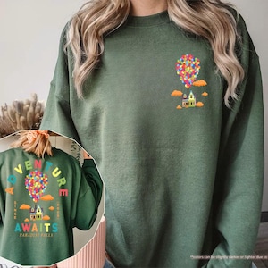 Puede incluir: Sudadera verde militar con un gr&aacute;fico colorido de una casa levantada por globos. La parte trasera de la sudadera presenta el texto "ADVENTURE AWAITS PARADISE FALLS" en un arco&iacute;ris, con el mismo dise&ntilde;o de casa y globos. Cuello redondo.