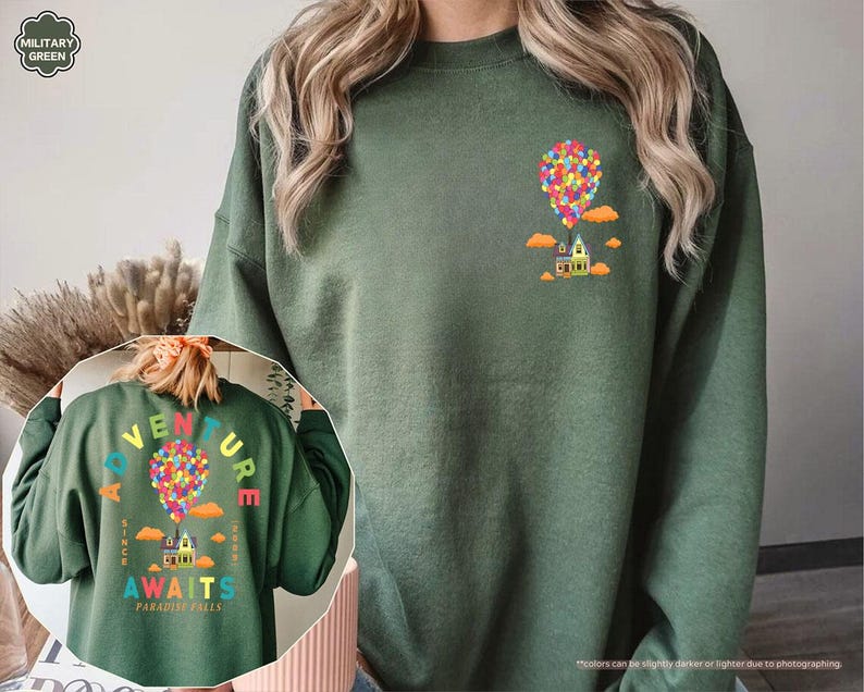Puede incluir: Sudadera verde militar con un gr&aacute;fico colorido de una casa levantada por globos. La parte trasera de la sudadera presenta el texto "ADVENTURE AWAITS PARADISE FALLS" en un arco&iacute;ris, con el mismo dise&ntilde;o de casa y globos. Cuello redondo.