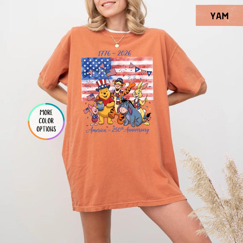 May include: Orange t-shirt featuring a graphic of Winnie the Pooh and friends in front of an American flag. The design includes the text "1776-2026" and "America - 250th Anniversary". The shirt is a relaxed fit.