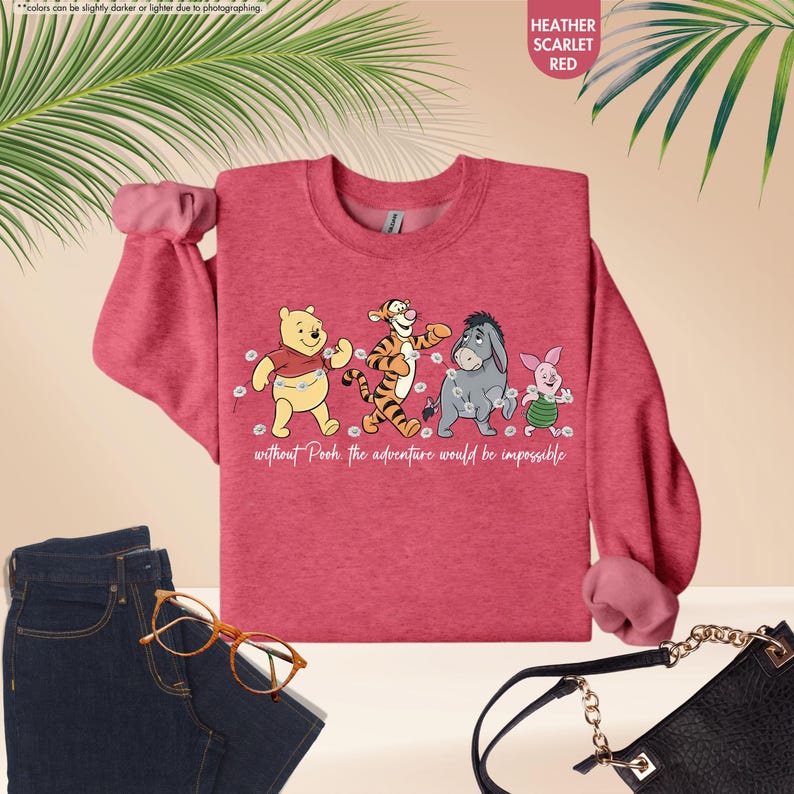 Puede incluir: Sudadera roja escarlata jaspeada con Winnie the Pooh, Tigger, Eeyore y Piglet. El texto "without Pooh the adventure would be impossible" est&aacute; impreso debajo de los personajes. La sudadera se combina con vaqueros azules y un bolso negro.