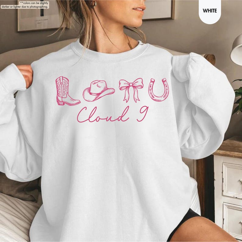 May include: White sweatshirt featuring a pink graphic of a cowboy boot, hat, bow, and horseshoe, with the text "Cloud 9" below. A casual, comfortable top, perfect for everyday wear. The design has a country theme.