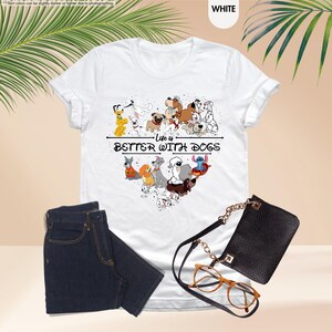 May include: White t-shirt with a heart-shaped graphic of various cartoon dogs and the text "Life is Better With Dogs." The shirt is paired with dark blue jeans, a black purse, and eyeglasses.