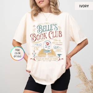 Pu&ograve; includere: T-shirt color avorio con la scritta "Belle's Book Club" in un design vintage. La grafica include una rosa in una cupola di vetro, un libro e la frase "Tale as old as Time". La maglietta presenta anche l'anno "1991" e la parola "EST."