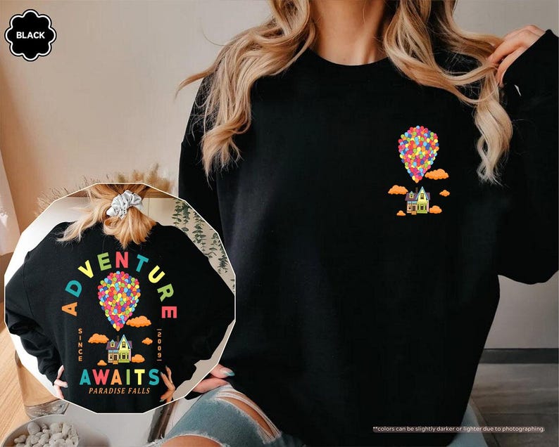 Puede incluir: Sudadera negra con un gr&aacute;fico colorido de una casa levantada por globos, con el texto "Adventure Awaits Paradise Falls" y el a&ntilde;o "2009". El dise&ntilde;o se repite en la espalda. La sudadera es negra.