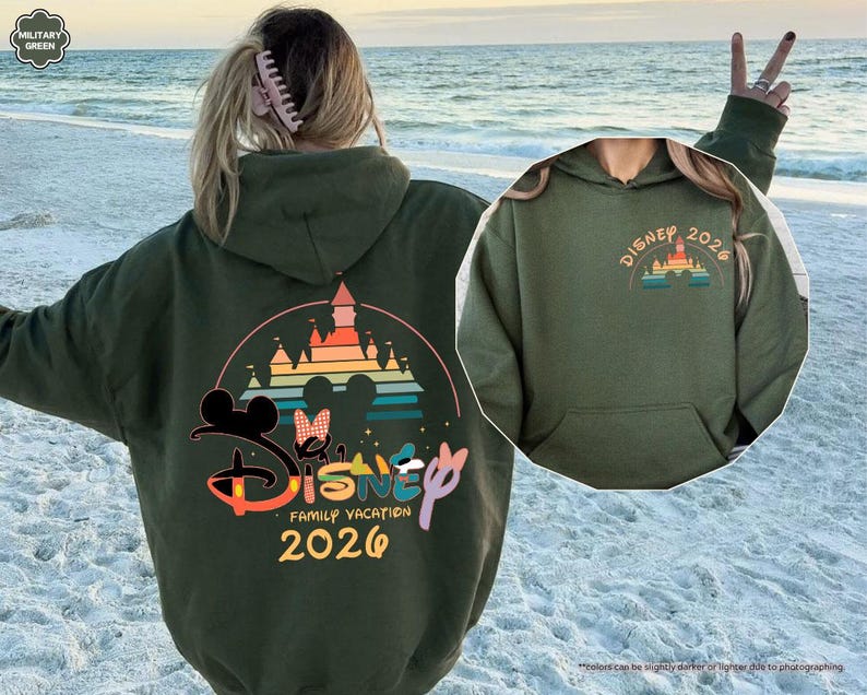 May include: An olive green hooded sweatshirt with a large graphic on the back featuring the Disney logo, Mickey and Minnie Mouse silhouettes, a castle, and the text "Disney Family Vacation 2026". A smaller graphic is on the front.