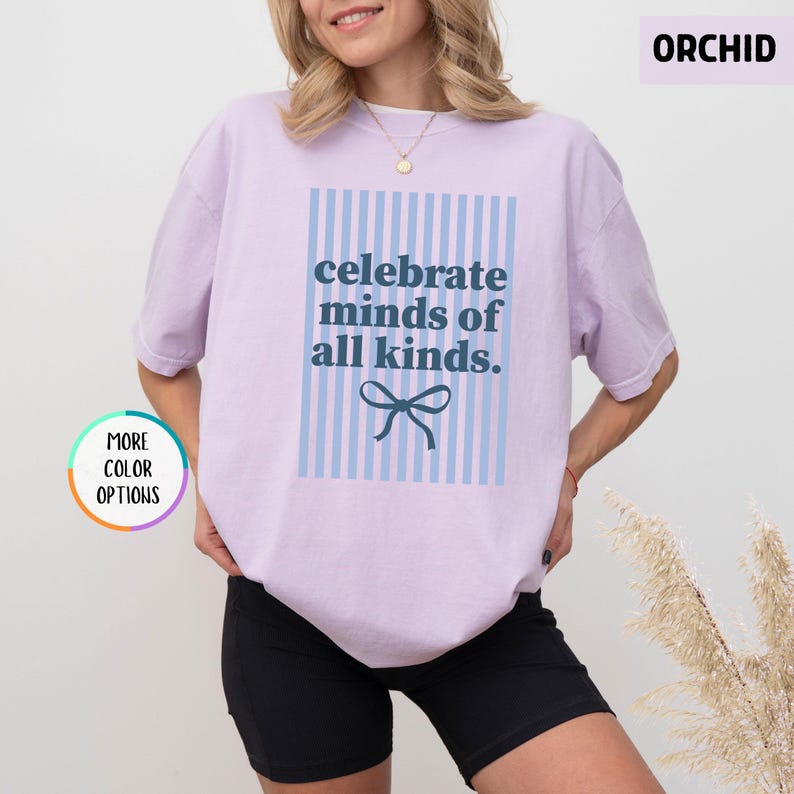 Puede incluir: Camiseta lila claro con el texto azul "celebrate minds of all kinds" sobre un fondo a rayas azul claro. Un lazo azul est&aacute; debajo del texto. La camiseta est&aacute; hecha de un material suave y c&oacute;modo.