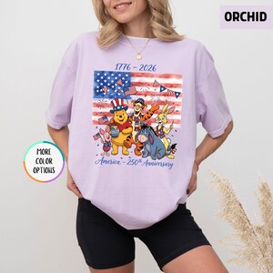 May include: Orchid-colored t-shirt featuring a graphic of Winnie the Pooh and friends celebrating the 250th anniversary of America. The design includes the American flag, fireworks, and the text "1776-2026" and "America - 250th Anniversary."